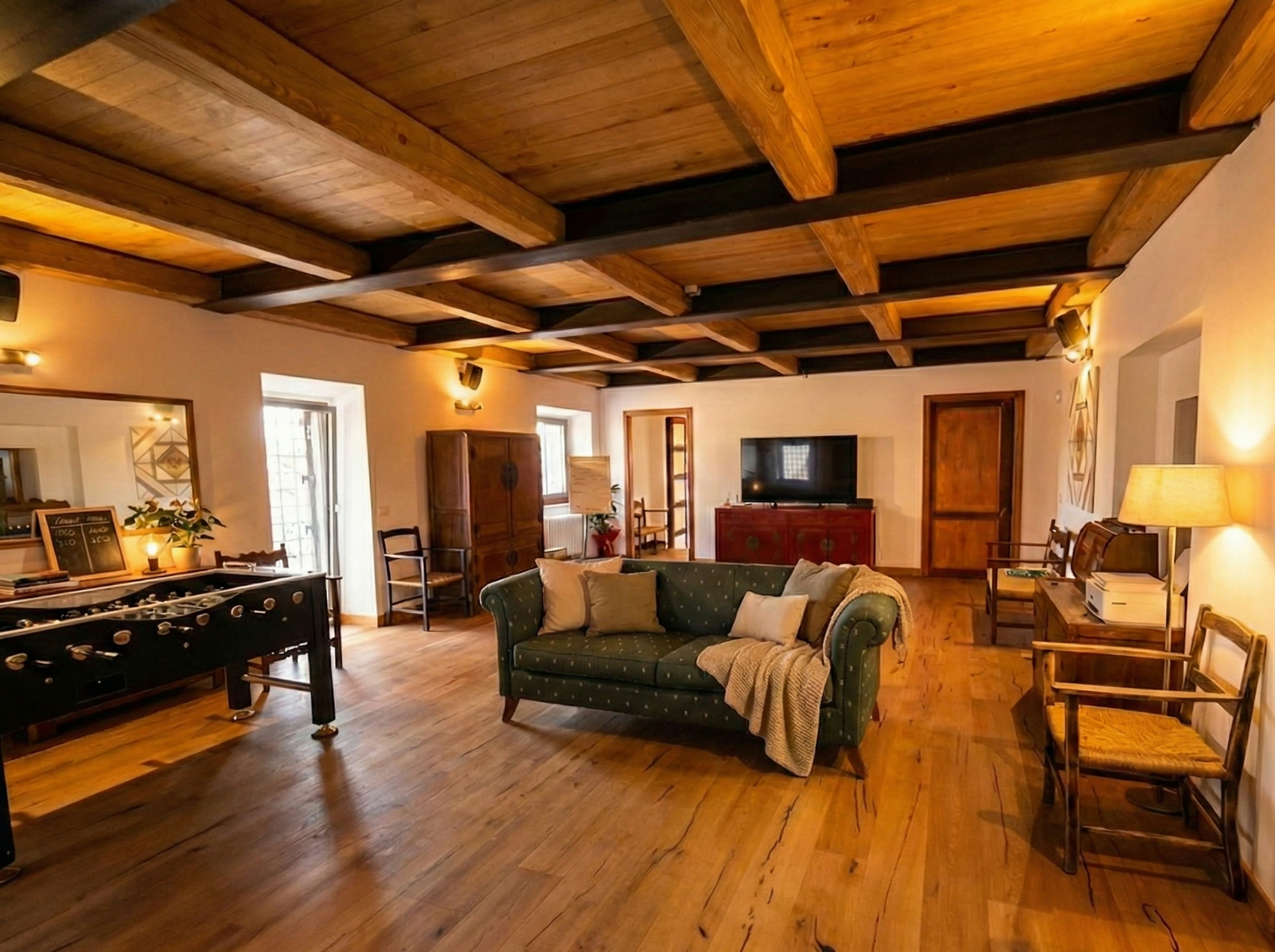 The beamed sitting room with foosball table, fireplace and green sofa