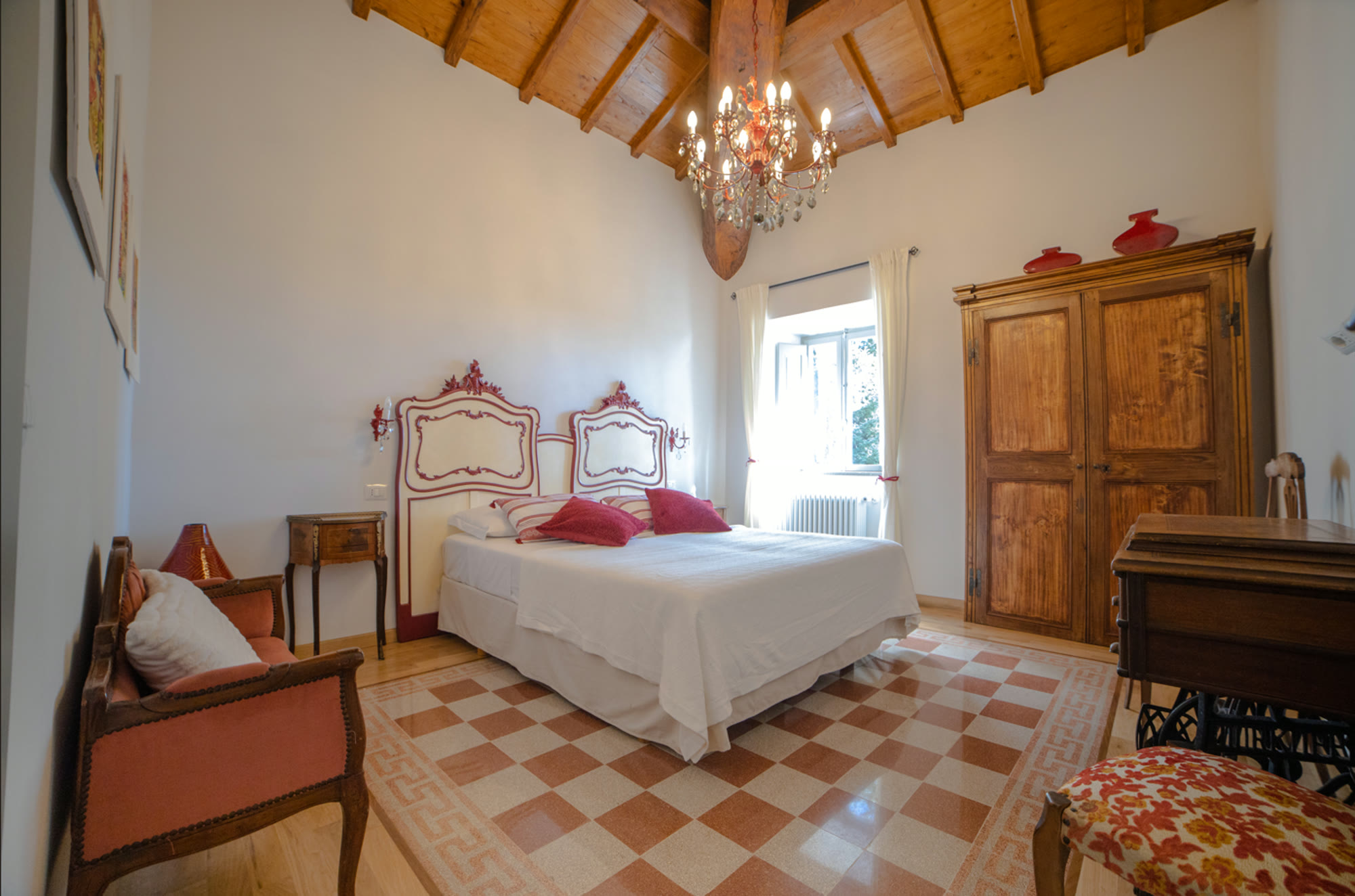 A bright room with carved headboards, chandelier and antique wardrobe over a chequered floor